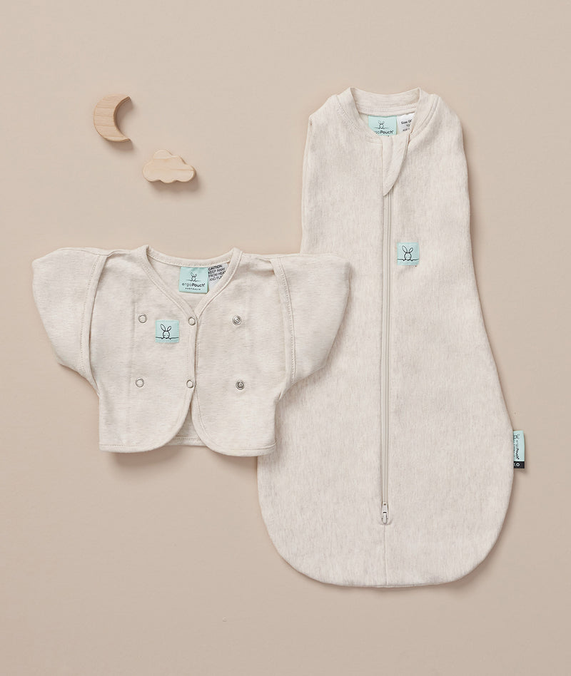Flatlay of a newborn essential starter kit including ergoPouch Cocoon Swaddle Sack 1.0 TOG and Butterfly Cardi in heritage color Oatmeal Marle 