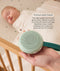 An adult hand holds a round, mint-green Drift Away white noise machine next to a crib where a baby is peacefully sleeping. A text box highlights 