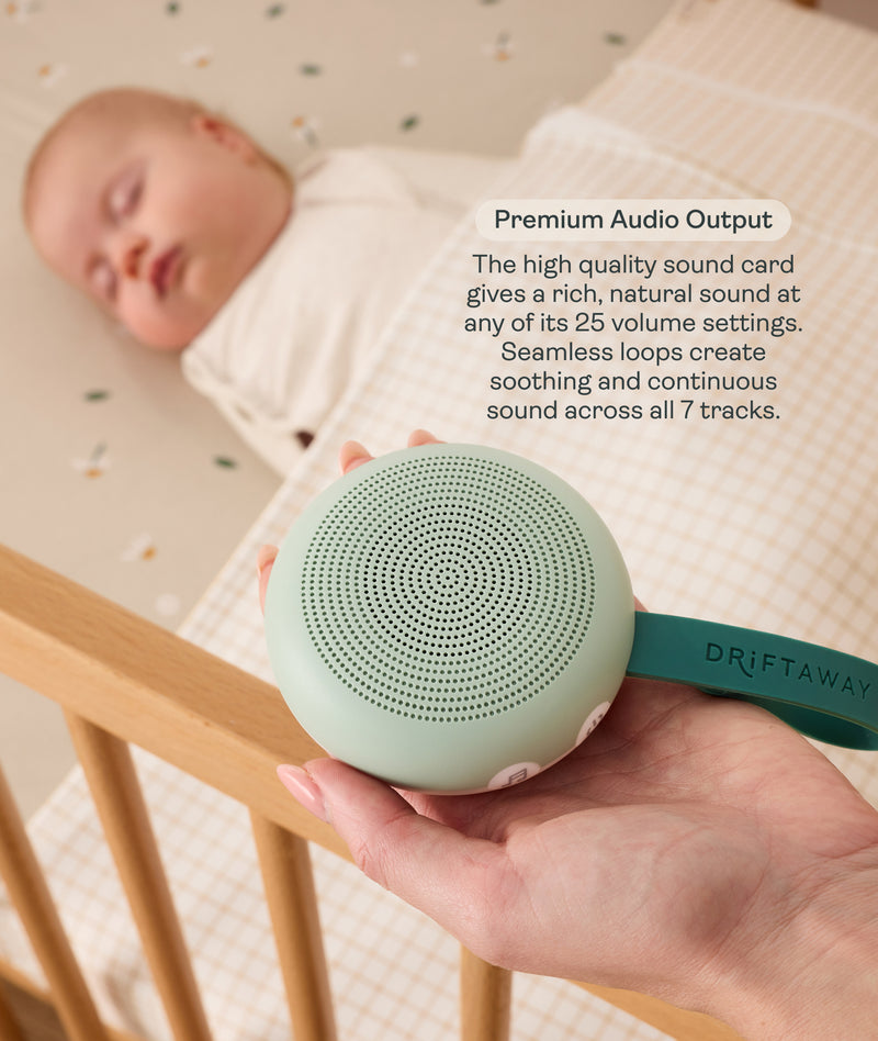 An adult hand holds a round, mint-green Drift Away white noise machine next to a crib where a baby is peacefully sleeping. A text box highlights 