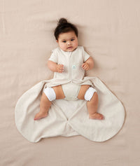 Baby lying in a Hip Harness Sleep Sack 0.2 TOG Oatmeal Marle with the bottom zip open