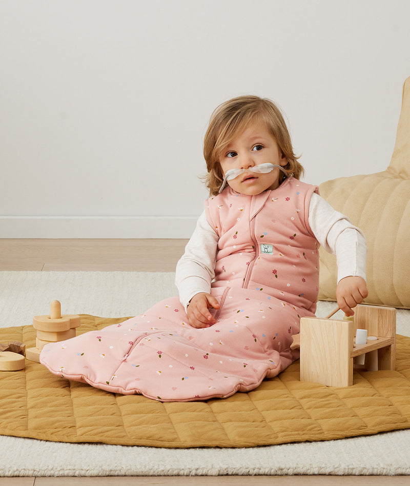 A child playing with toys in an ergoPouch Sleep Sack 2.5 TOG Daisies layered with a Long Sleeve Romper 1.0 TOG Oatmeal Marle underneath to keep warm in the winter months. 