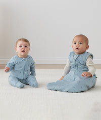 Two infants sitting on the floor both wearing ergPouch Dragonflies, one in a Long Sleeve Romper 1.0 TOG and the other in a Sleep Sack 2.5 TOG, perfect layering for the colder months