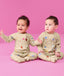 Two infants sitting on the floor wearing ergoPouch Long Sleeve Romper 0.2 TOG in Birthday Blobs 