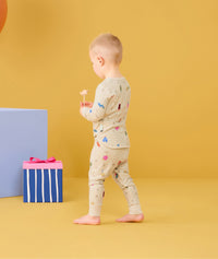 Toddler walking away with candy in his hand wearing ergoPouch Long Sleeve Pajamas 0.2 TOG in Birthday Blobs 