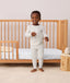 A toddler wearing ergoPouch Long Sleeve Pajamas standing next to a toddler bed.
