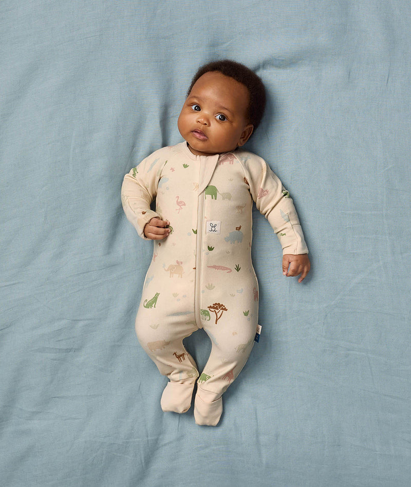 Baby lying in bed wearing ergoPouch Long Sleeve Romper 1.0 TOG Savannah with foot cuffs folded over.