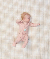 Baby lying in bed dressed in ergoPouch Long Sleeve Romper 1.0 TOG Daisies