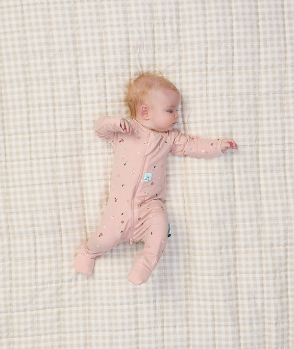 Baby lying in bed dressed in ergoPouch Long Sleeve Romper 1.0 TOG Daisies
