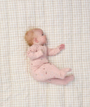 Baby lying on a beige checkered blanket, wearing a light pink ergoPouch Long Sleeve Romper with small floral prints.