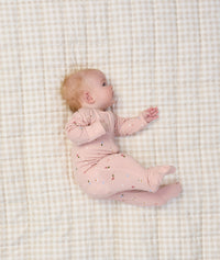 Baby lying on a beige checkered blanket, wearing a light pink ergoPouch Long Sleeve Romper with small floral prints.