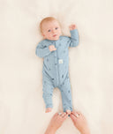 A parent is putting the baby in an ergoPouch Long Sleeve Romper, folding the foot cuffs for added warmth.