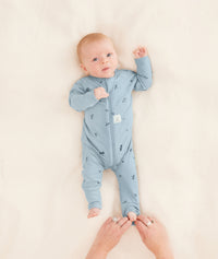 A parent is putting the baby in an ergoPouch Long Sleeve Romper, folding the foot cuffs for added warmth.