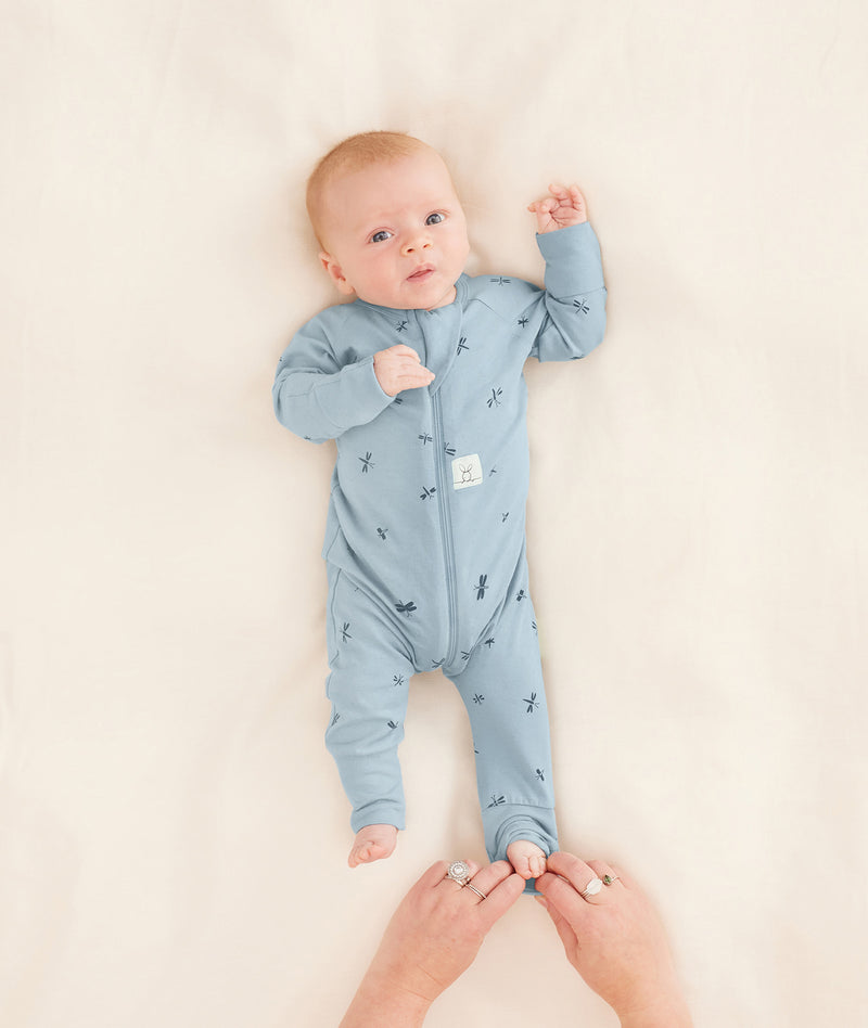 A parent is putting the baby in an ergoPouch Long Sleeve Romper, folding the foot cuffs for added warmth.
