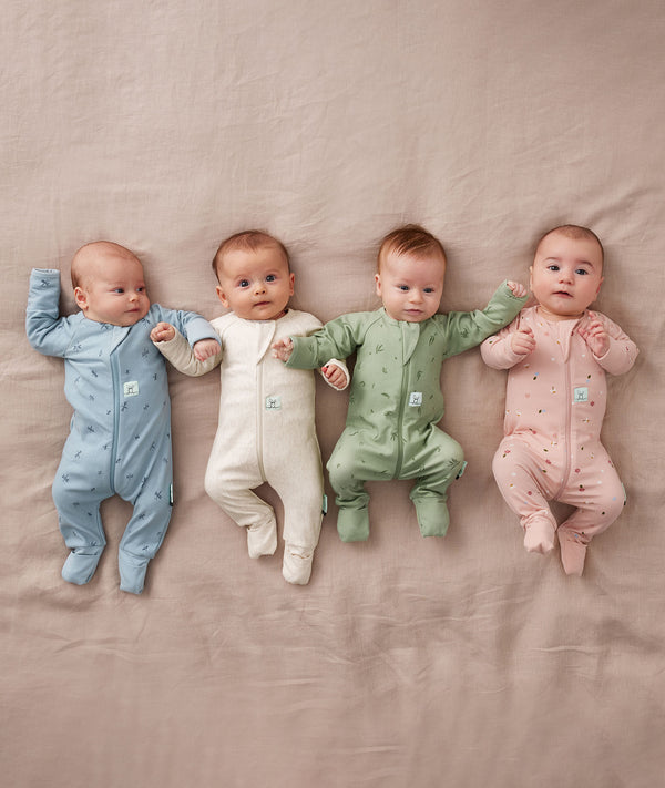 Four babies lying side by side, each wearing ergoPouch Long Sleeve Rompers in Dragonflies, Oatmeal Marle, Willow, and Daisies.