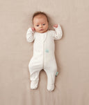 Baby lying in a neutral color blanket wearing an ergoPouch Long Sleeve Romper with its foot cuffs folded over for extra warmth and protection.