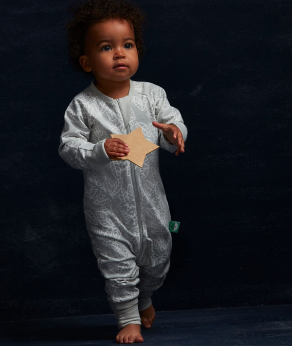 Toddler dressed in a light grey, long-sleeved one-piece romper adorned with a delicate white leaf pattern. The romper features a central zipper and ribbed cuffs at the ankles.