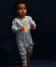 Toddler dressed in a light grey, long-sleeved one-piece romper adorned with a delicate white leaf pattern. The romper features a central zipper and ribbed cuffs at the ankles.