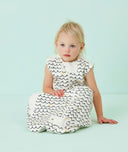 Infant wearing a white sleeveless sleep sack featuring a wave pattern, sitting against a light blue background.