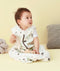 Baby wearing a white sleep sack featuring clouds pattern and front zipper, sitting against a beige background.