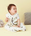 Baby wearing a white sleep sack featuring clouds pattern and front zipper, sitting against a beige background.