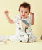 Baby wearing a white sleep sack featuring clouds pattern and front zipper, sitting against a beige background while holding a toy camera