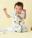 Baby wearing a white sleep sack featuring clouds pattern and front zipper, sitting against a beige background while holding a toy camera