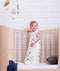 Baby standing on a crib wearing a premium sleep sack featuring clouds pattern