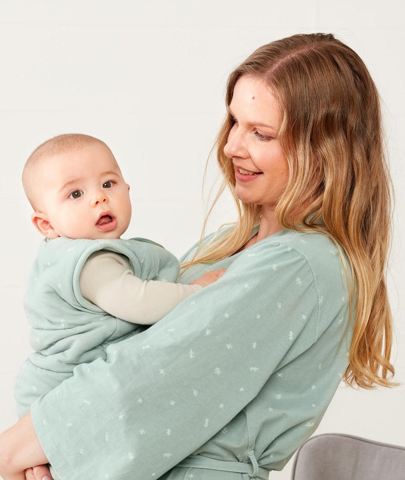 Mom holding baby wearing an ergoPouch Matchy Matchy Robe Sage