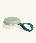 Portable white noise machine with a soft green silicone exterior,  white control buttons, a built-in night light at the base, and a flexible dark green loop handle for hanging or carrying.