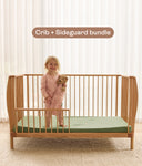 Child standing on ergoPouch ellska Skye Crib that has converted to a toddler bed, holding a teddy bear.