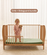 Child standing on ergoPouch ellska Skye Crib that has converted to a toddler bed, holding a teddy bear.