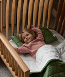 Toddler lying on the ergoPouch ellska Skye Crib that has converted into a toddler bed, made to grow with your family.