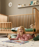 Child lying on the floor in a nursery with  the ergoPouch ellska Skye Crib in the background, a promise of safety and serenity