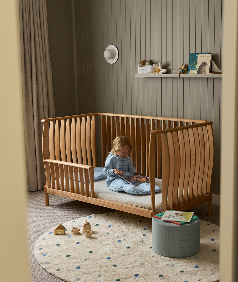 Toddler reading her book, sitting on the ergoPouch ellska Skye Crib converted into a toddler bed, supporting a smooth big-bed transition.