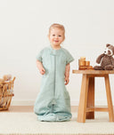 Smiling child in ergoPouch Sleep Suit Sack 1.0 TOG Sage, a sleep sack with legs