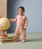 A toddler stands beside a globe, wearing an ergoPouch Sleep Onesie 2.5 TOG in Elephant Parade.