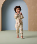 A toddler walks barefoot while smiling and holding sunglasses, 2.5 TOG Sleep Onesie with long sleeves and full-length legs. The onesie features playful animal prints and a front zipper, designed for warmth, mobility, and all-day comfort.