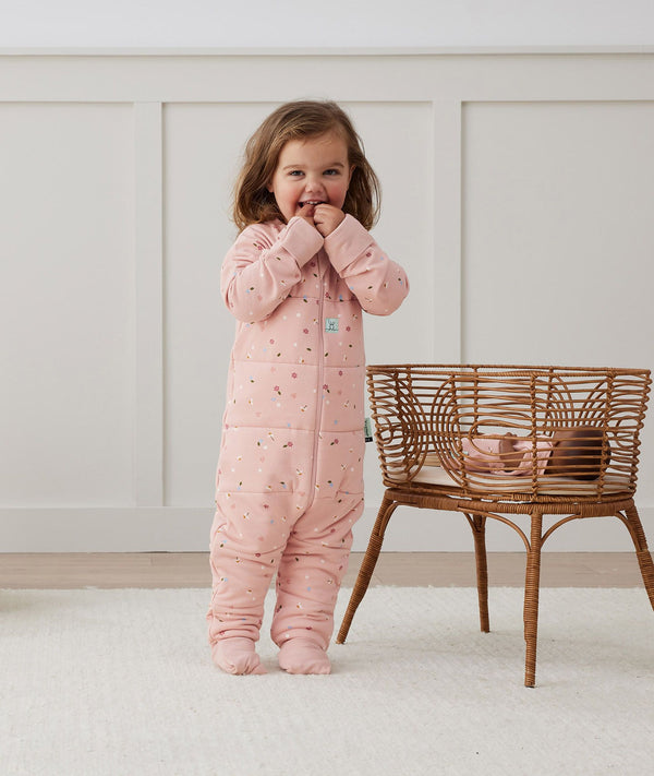 Toddler playing with baby doll in bassinet, wearing an ergoPouch Sleep Onesie 2.5 TOG Daisies