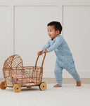 Toddler playing with baby doll in bassinet, wearing an ergoPouch Sleep Onesie 2.5 TOG Daisies