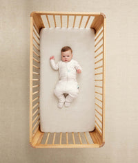 Child lying in crib wearing an ergoPouch Sleep Onesie 2.5 TOG Oatmeal Marle