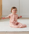 Child sitting in ergoPouch Jersey Sleep Suit Sack 0.2 TOG Daisies, a light sleeping bag that converts to a sleeping bag with legs