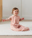 Child sitting in ergoPouch Jersey Sleep Suit Sack 0.2 TOG Daisies, a light sleeping bag that converts to a sleeping bag with legs