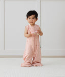 Toddler wearing an ergoPouch Sleep Suit Sack 0.2 TOG Daisies, holding a wooden toy