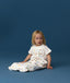 Toddler sitting in an ergoPouch Sleep Suit Sack 1.0 TOG Daydream, a sleep sack that converts to a sleep suit with legs by a four-way zipper feature. 