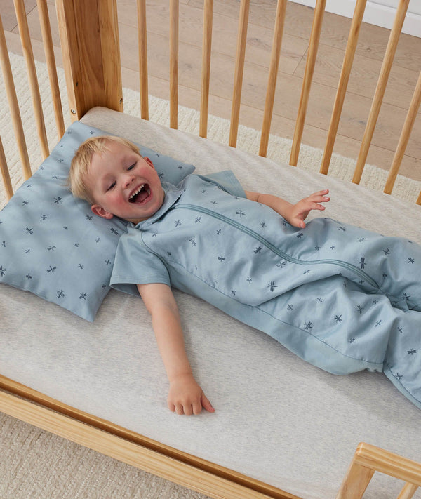 Toddler lying in crib on a ergoPouch Organic Toddler Pillow And Case Dragonflies, designed to support the correct alignment of the neck during sleep