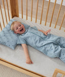 Toddler lying in an ergoPouch Sleep Suit Sack 1.0 TOG Dragonflies, a sleeping bag that converts to a sleeping bag with legs