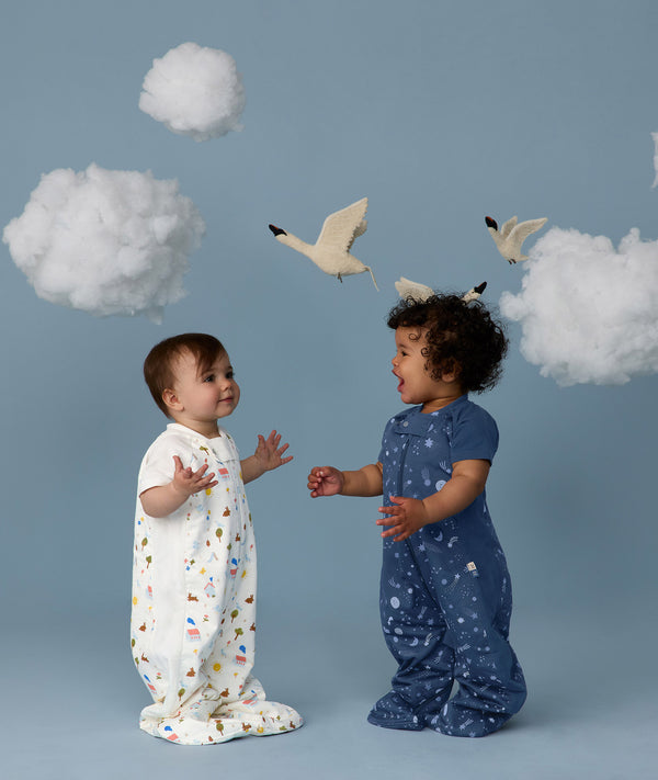 Two children wearing ergoPouch Sleep Suit Sack 1.0 TOG Daydream and Starbeam, a sleep sack that converts to a sleep suit with legs by a four-way zipper feature. 