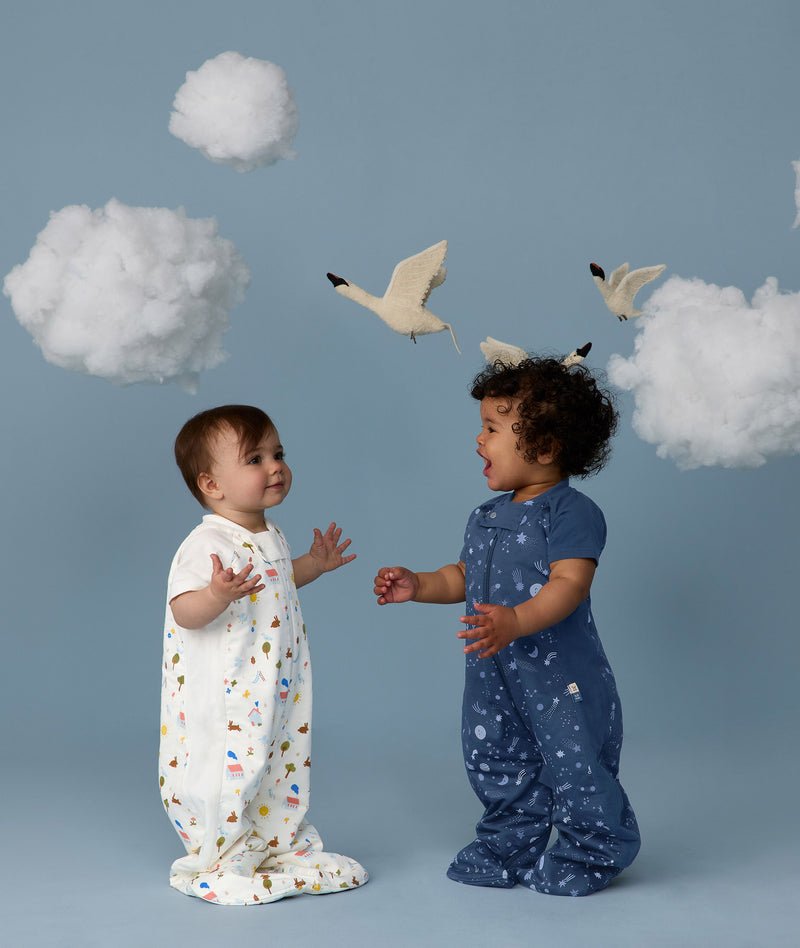 Two children wearing ergoPouch Sleep Suit Sack 1.0 TOG Daydream and Starbeam, a sleep sack that converts to a sleep suit with legs by a four-way zipper feature. 