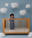 Child standing in a wooden crib wearing an ergoPouch Sleep Suit Sack 1.0 TOG Starbeam, a sleeping bag that converts to a sleep suit with legs.
