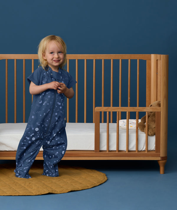 Toddler wearing an ergoPouch Sleep Suit Sack 1.0 TOG Starbeam, a sleeping bag that converts to a sleep suit with legs.